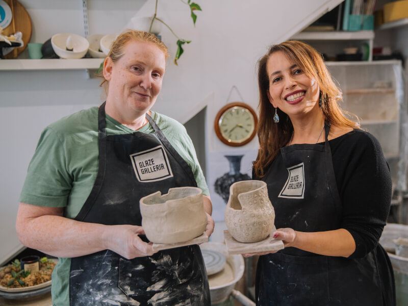 Two women smiling and holding up ceramic pieces